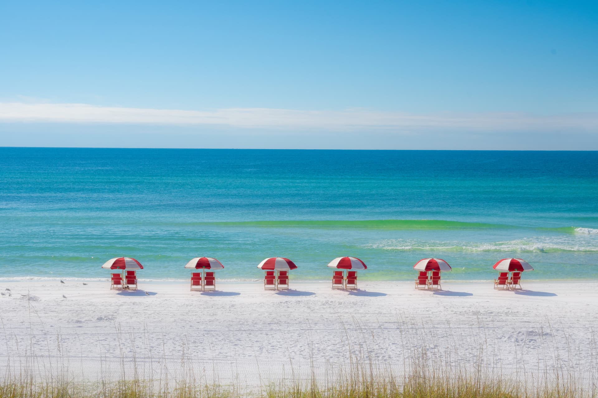 Rows of red and white beach umbrellas on the white sand of Destin, Florida, beside turquoise Gulf water